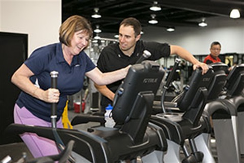 Trainer helping someone use gym equipment. 