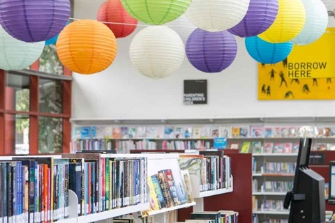 Books lining the shelves of a library with colourful lanterns hanging from the ceiling 